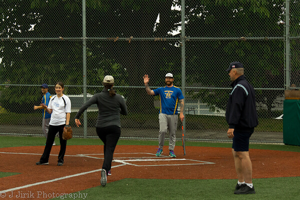 Adult players running and fielding at home plate during a co-ed softball game in Seattle Parks.