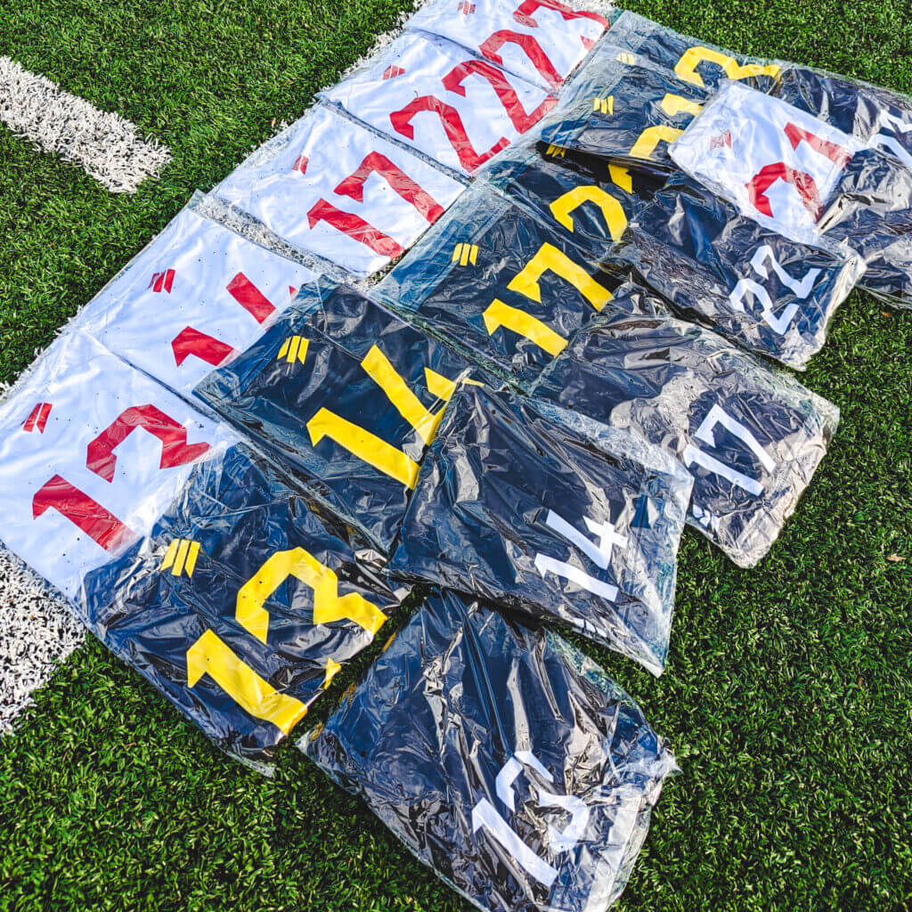 Individually packed custom jerseys with printed numbers, showing home and away sets on a turf field.