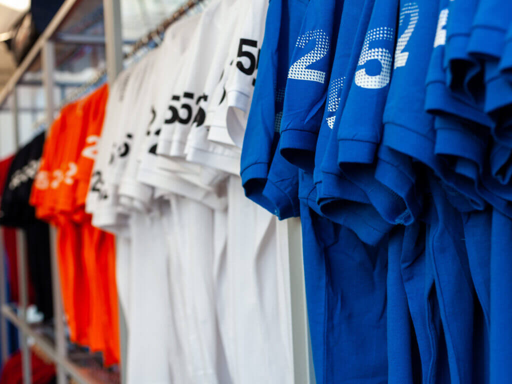Rows of custom sports jerseys in blue, white, and orange hanging on a rack with printed numbers on the sleeves.