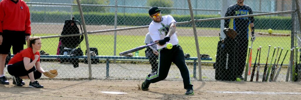slow pitch softball Seattle Tacoma game with batter swinging and catcher ready behind the plate